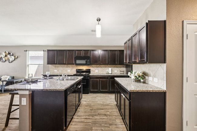 Kitchen with black appliances, light wood-style flooring, dark brown cabinetry, and backsplash | Image 7