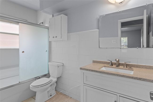 Full bathroom featuring vanity, tile walls, tile patterned flooring, and shower / bath combination with glass door | Image 15