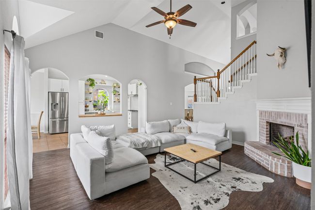 Living room featuring a ceiling fan, high vaulted ceiling, stairs, arched walkways, and a brick gas fireplace | Image 19
