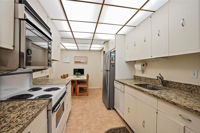 Kitchen with sink, dark stone countertops, stainless steel appliances, and white cabinetry | Image 10