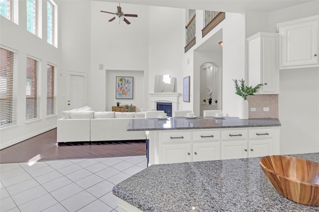 Kitchen featuring dark stone countertops, a towering ceiling, tile patterned floors, ceiling fan, and white cabinetry | Image 5