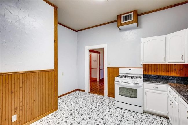 Kitchen featuring white gas range, wainscoting, white cabinets, ornamental molding, and wooden walls | Image 10