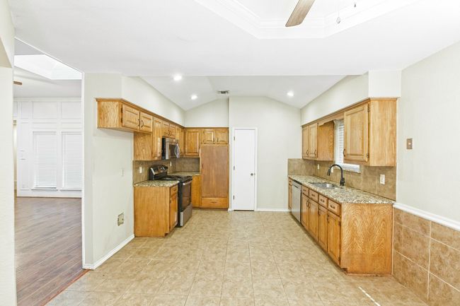 Kitchen with appliances with stainless steel finishes, light stone countertops, recessed lighting, decorative backsplash, and brown cabinets | Image 11
