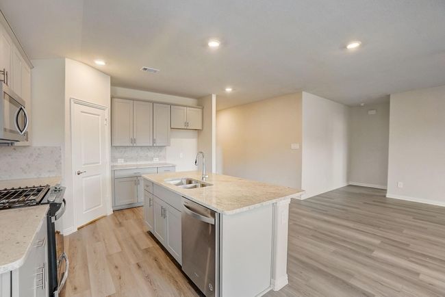 Kitchen featuring light wood-type flooring, stainless steel appliances, backsplash, light stone countertops, and recessed lighting | Image 21