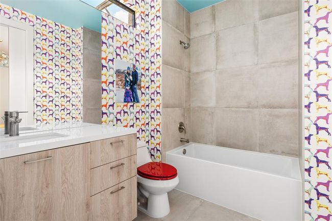 This vibrant Jack & Jill bath makes a bold statement with Milton & King’s playful dog-print wallpaper, bringing personality and fun to the space. Concrete-look tile surrounds the tub and shower, creating a modern contrast to the colorful walls, while the light wood vanity and sleek fixtures keep the look polished and fresh. | Image 23