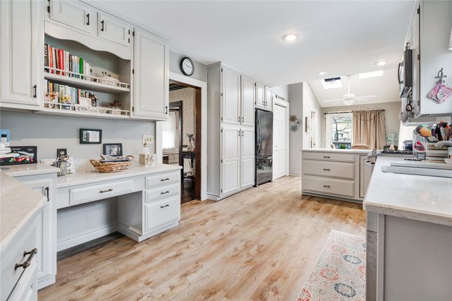 Kitchen featuring light wood-type flooring, freestanding refrigerator, built in desk, white cabinetry, and a skylight | Image 8