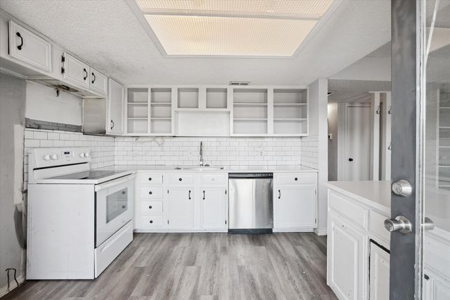 Kitchen with white range with electric cooktop, white cabinetry, decorative backsplash, and a textured ceiling | Image 7