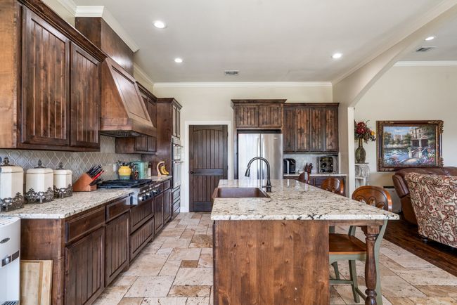 Kitchen with appliances with stainless steel finishes, stone tile flooring, an island with sink, a breakfast bar area, and light stone counters | Image 15