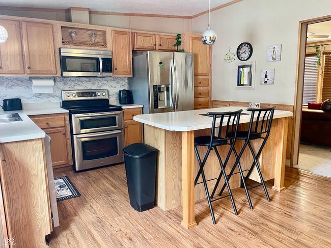 kitchen featuring stainless steel appliances, light wood finished floors, a kitchen bar, and light countertops | Image 5