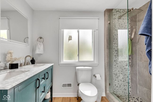Full primary suite bathroom featuring double vanity, a shower stall, toilet, and wood finished floors. | Image 30