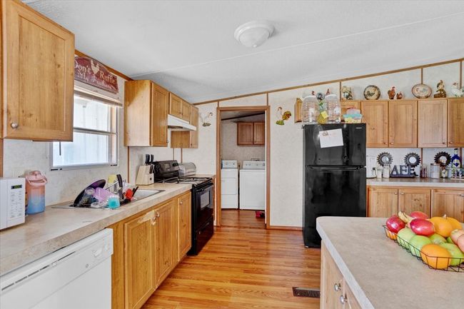 Kitchen with washing machine and dryer, under cabinet range hood, light countertops, black appliances, and light wood finished floors | Image 10