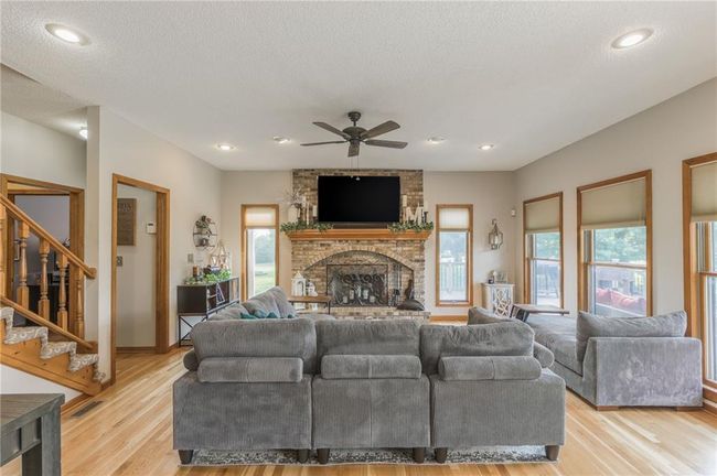 Living room with light wood-style flooring, a brick fireplace, stairway, baseboards, and ceiling fan | Image 40