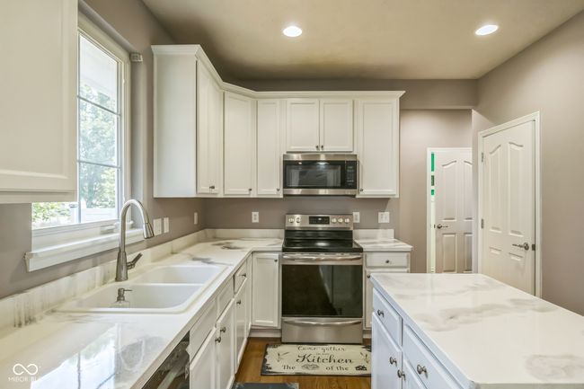 kitchen featuring appliances with stainless steel finishes, white cabinets, recessed lighting, light stone counters, and dark wood-style floors | Image 10