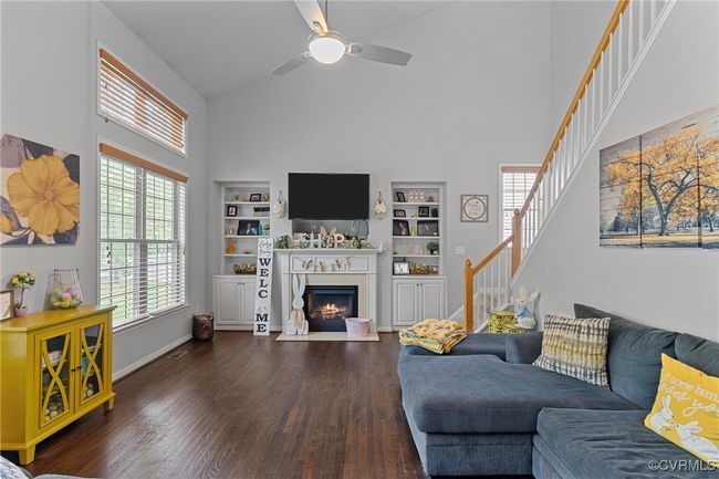 Living room with a fireplace with flush hearth, wood finished floors, a ceiling fan, high vaulted ceiling, and stairs | Image 16