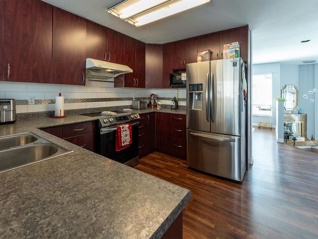 Kitchen with tasteful backsplash, under cabinet range hood, dark countertops, dark wood-style floors, and appliances with stainless steel finishes | Image 10
