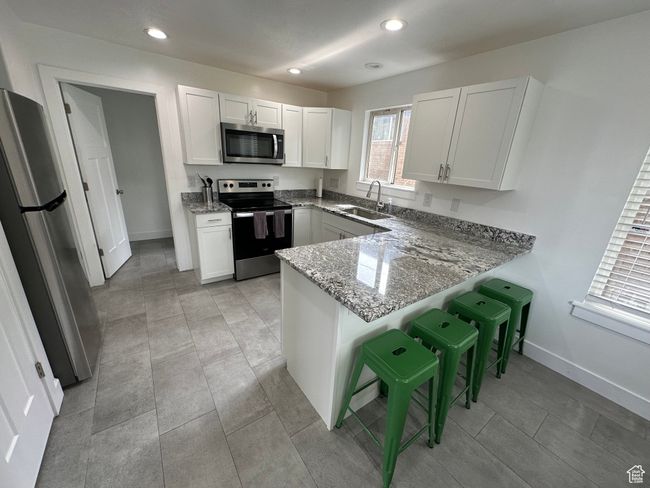 Kitchen with stainless steel appliances, a sink, a peninsula, light stone countertops, and baseboards | Image 20