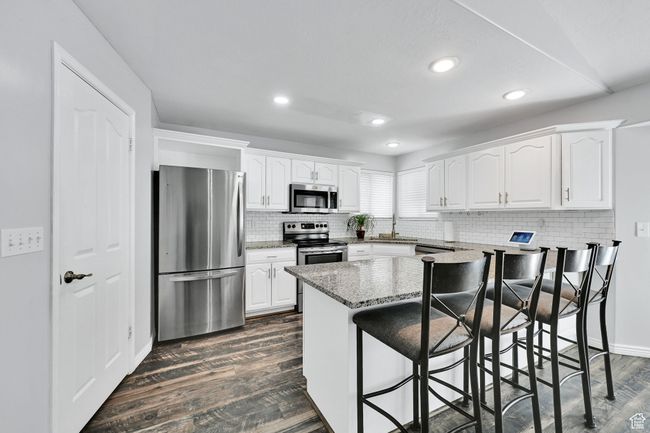 Kitchen with white cabinets, stainless steel appliances, dark wood-type flooring, light stone counters, and a kitchen breakfast bar | Image 14