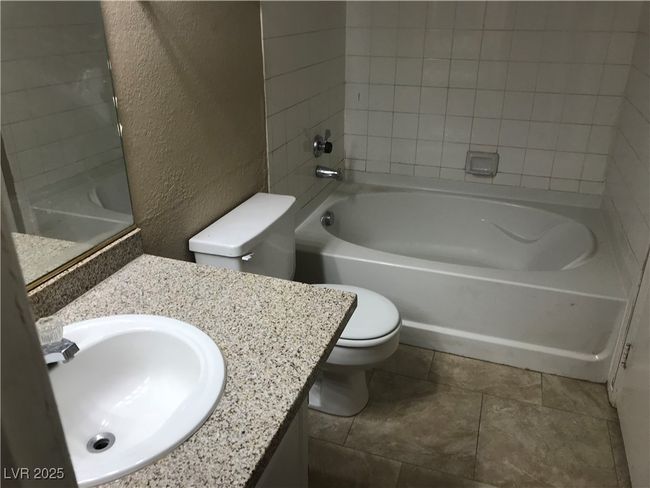Full bathroom with a textured wall, toilet, vanity, bathing tub / shower combination, and tile patterned flooring | Image 8