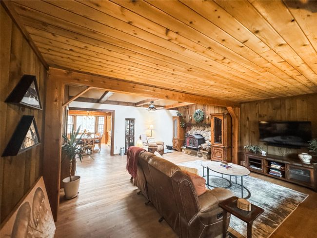 Living room featuring a fireplace, a ceiling fan, wooden walls, wood finished floors, and wooden ceiling | Image 6