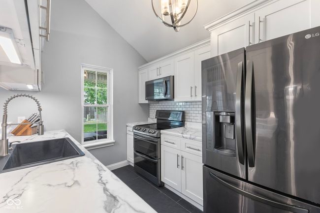 kitchen with stainless steel appliances, lofted ceiling, backsplash, white cabinets, and light stone countertops | Image 10