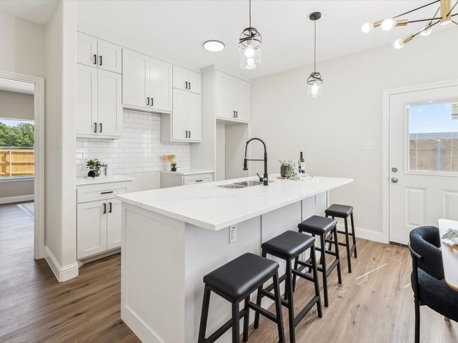 Kitchen featuring white cabinets, light wood finished floors, a sink, baseboards, and tasteful backsplash | Image 9
