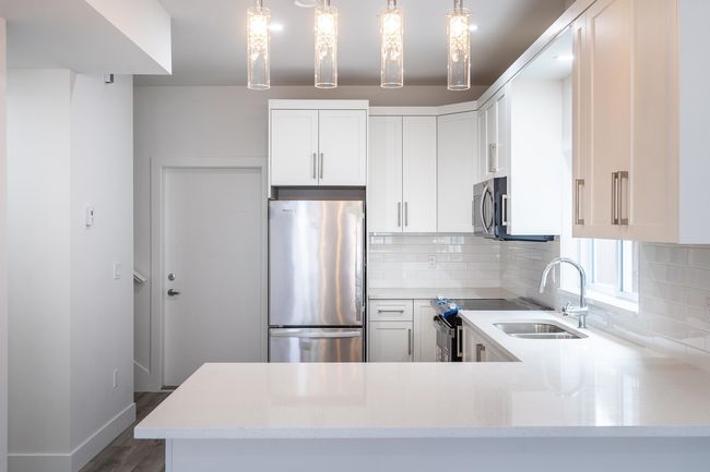 Kitchen featuring appliances with stainless steel finishes, backsplash, a peninsula, a sink, and white cabinetry | Image 7