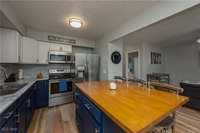 Kitchen featuring stainless steel appliances, blue cabinetry, light wood-type flooring, white cabinets, and a textured ceiling | Image 8
