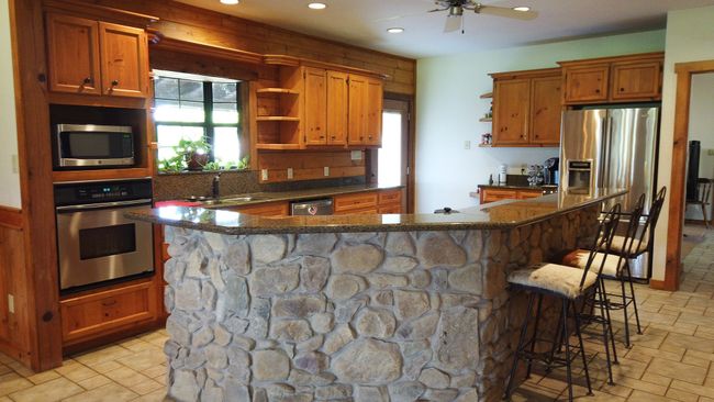 Kitchen featuring a kitchen breakfast bar, brown cabinetry, open shelves, recessed lighting, and appliances with stainless steel finishes | Image 14