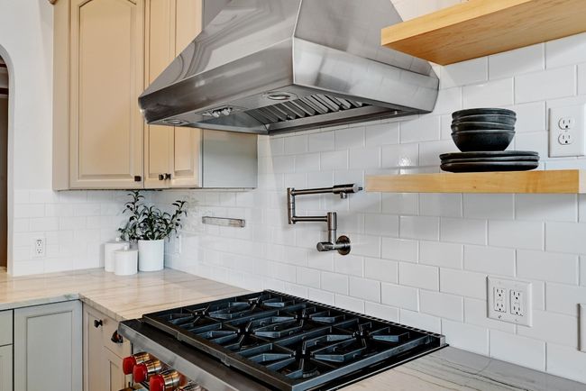 Kitchen featuring Wolf 6-burner range, pot-filler, Quartzite stone counters, range hood, decorative backsplash, and arched walkways | Image 12
