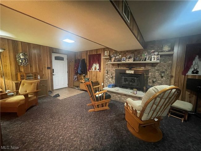 Living area with carpet floors, wooden walls, a fireplace, and a wood stove | Image 22