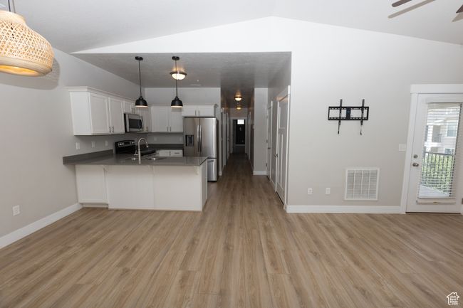 Kitchen featuring stainless steel appliances, a peninsula, light wood-style flooring, white cabinetry, and a sink | Image 4
