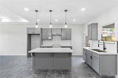 Kitchen with hanging light fixtures, sink, gray cabinets, a center island, and decorative backsplash | Image 2