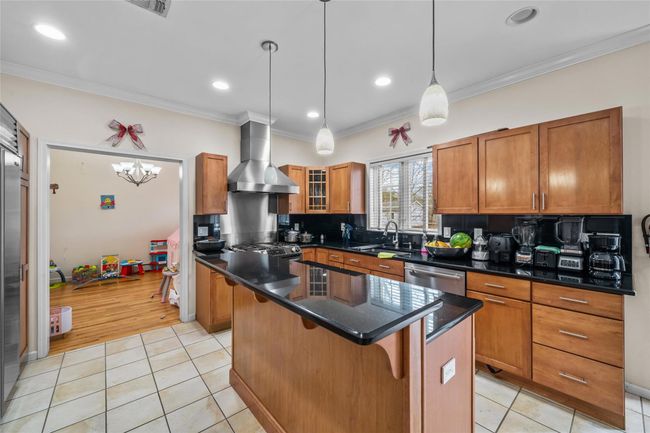 Kitchen featuring a center island, brown cabinets, wall chimney exhaust hood, appliances with stainless steel finishes, and a sink | Image 12