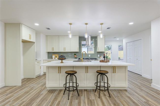 The breakfast bar on one side of the island is perfect for casual meals, offering seating for family and guests while allowing for easy conversation with the cook. The Quartz countertops extend across the island, complemented by the sleek green subway tile backsplash. | Image 11
