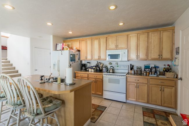 Kitchen with light tile patterned floors, a sink, a kitchen bar, white appliances, and a center island with sink | Image 10