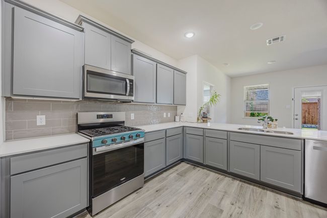 Kitchen with appliances with stainless steel finishes, gray cabinets, light wood-style floors, light countertops, and decorative backsplash | Image 7