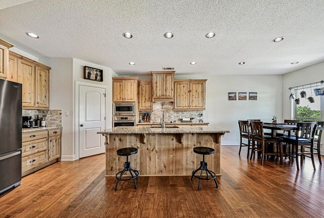 Kitchen with stainless steel appliances, backsplash, dark wood finished floors, light stone counters, and a breakfast bar | Image 9