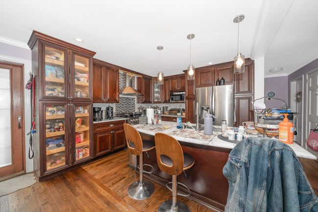 Kitchen featuring stainless steel appliances, wall chimney range hood, a kitchen breakfast bar, dark wood-type flooring, and backsplash | Image 24