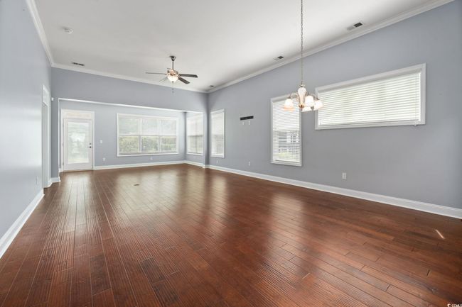 Unfurnished living room featuring baseboards, visible vents, ceiling fan with notable chandelier, and crown molding | Image 11