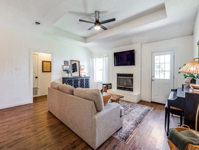 Living room with a tray ceiling, a brick fireplace, a ceiling fan, and dark wood-type flooring | Image 5