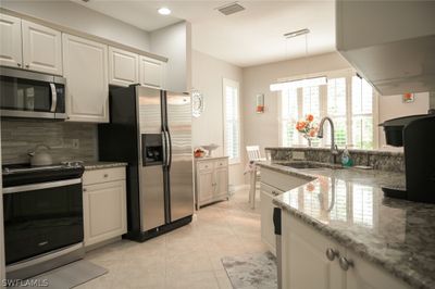 Kitchen with stainless steel appliances, sink, decorative light fixtures, backsplash, and light tile patterned floors | Image 3