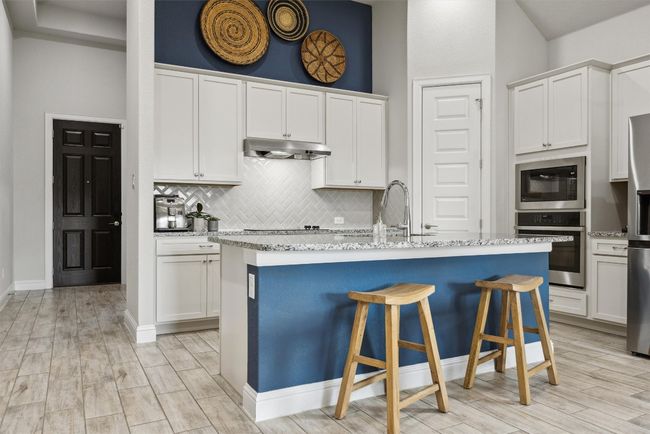 Kitchen with appliances with stainless steel finishes, under cabinet vent hood, tasteful backsplash, white cabinetry, and a breakfast bar area | Image 8
