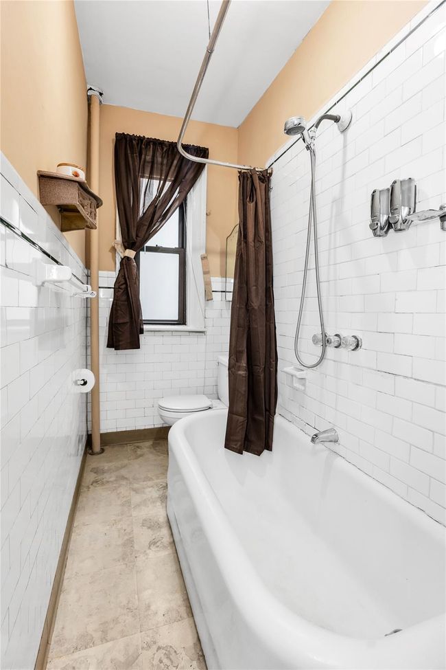 Full bath featuring toilet, tile walls, shower / bath combo with shower curtain, and wainscoting | Image 11