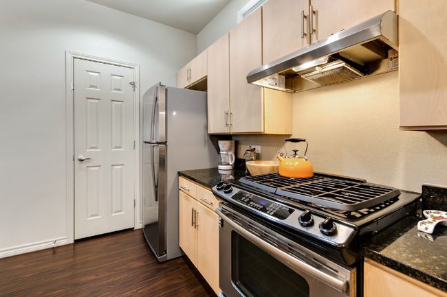 Kitchen with appliances with stainless steel finishes, under cabinet range hood, dark wood-style flooring, and dark stone countertops | Image 18
