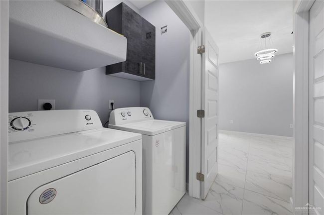 Laundry room featuring light marble finish flooring, washing machine and dryer, and baseboards | Image 8