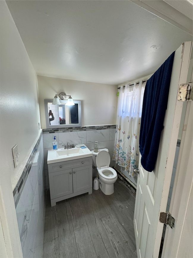 Full bathroom featuring a wainscoted wall, toilet, tile walls, wood finished floors, and vanity | Image 18