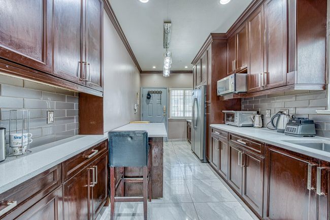 Kitchen featuring appliances with stainless steel finishes, ornamental molding, light marble finish flooring, tasteful backsplash, and light countertops | Image 9