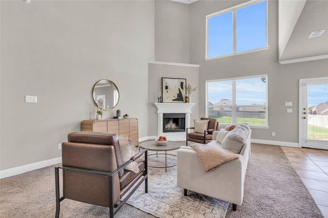 Living room featuring baseboards, a high ceiling, a fireplace with raised hearth, light carpet, and light tile patterned floors | Image 11