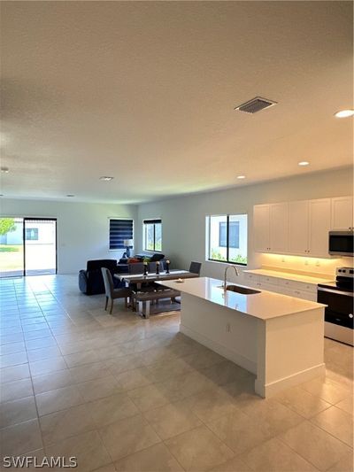 Kitchen with light tile flooring, stove, an island with sink, white cabinets, and sink | Image 3