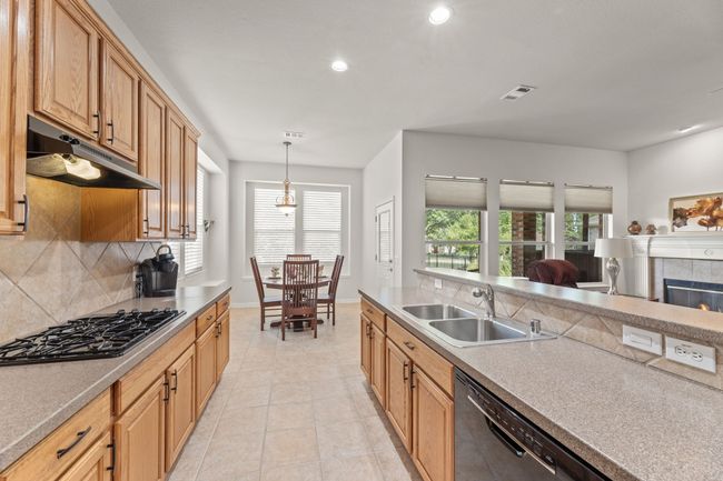 Kitchen with a sink, dishwashing machine, black gas stovetop, under cabinet range hood, and decorative backsplash | Image 20